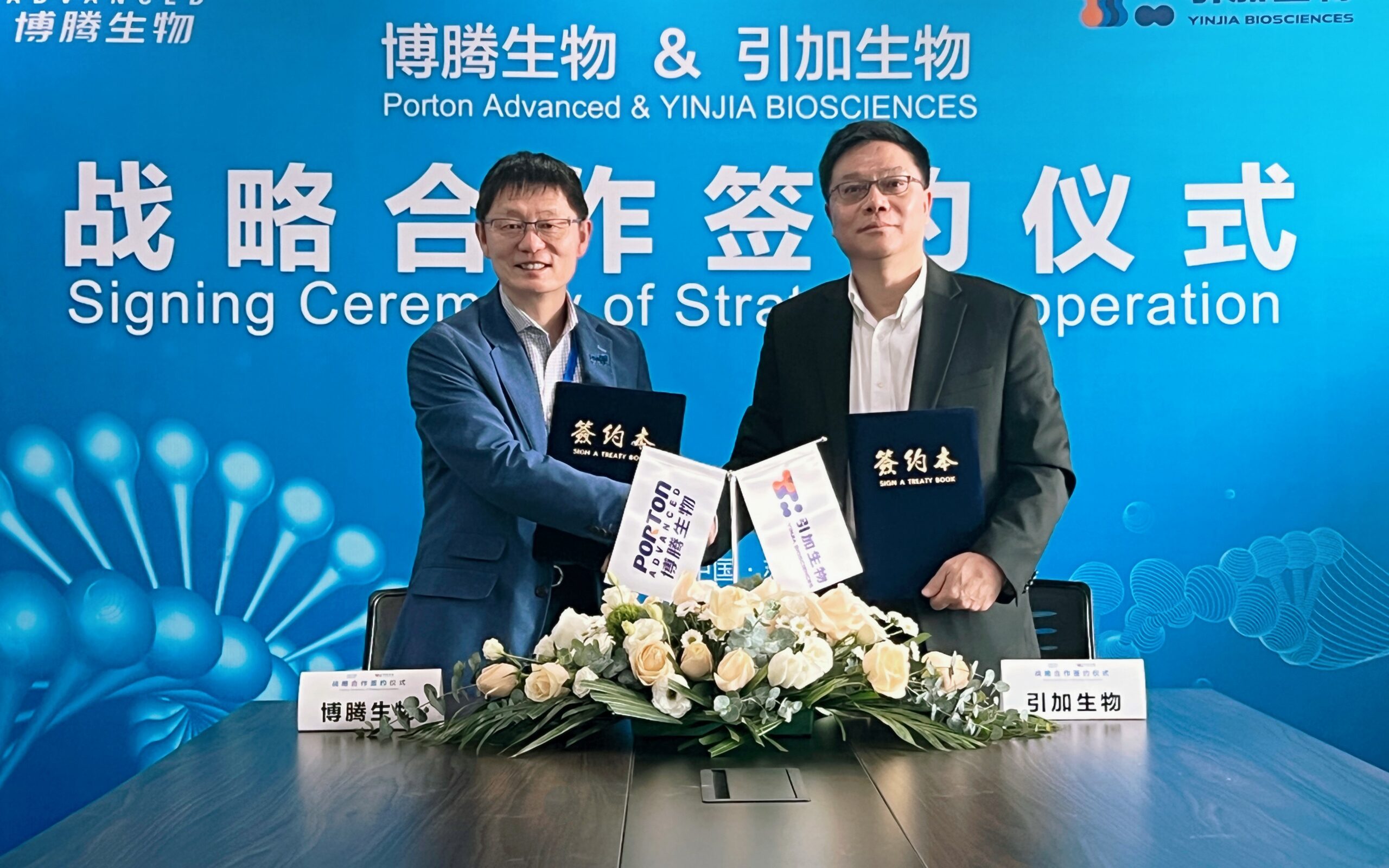 Two men in suits standing in front of a blue table.